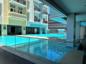 A modern hotel pool area with clear blue water, sun loungers, and a glass railing. - St Dominic (Iloilo)