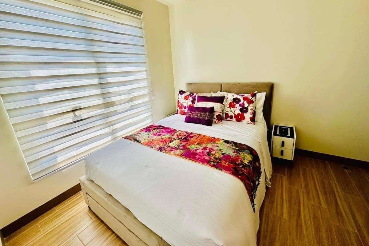 A bedroom with a bed, a nightstand, and a window with blinds.