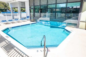 Ein rechteckiger Swimmingpool mit einer Metallleiter, umgeben von weißen Geländern und blauen Liegestühlen.