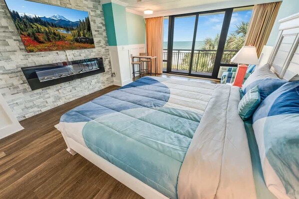 Ein Schlafzimmer mit einem großen Bett, einem an der Wand befestigten Fernseher, einem Balkon mit Meerblick und einem kleinen Tisch mit Stühlen.
