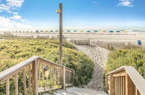 A beach with wooden walkways, a sandy path, and beach umbrellas in the background. - Newly Remodeled, Caravelle Resort, Amazing Pools! (Myrtle Beach)
