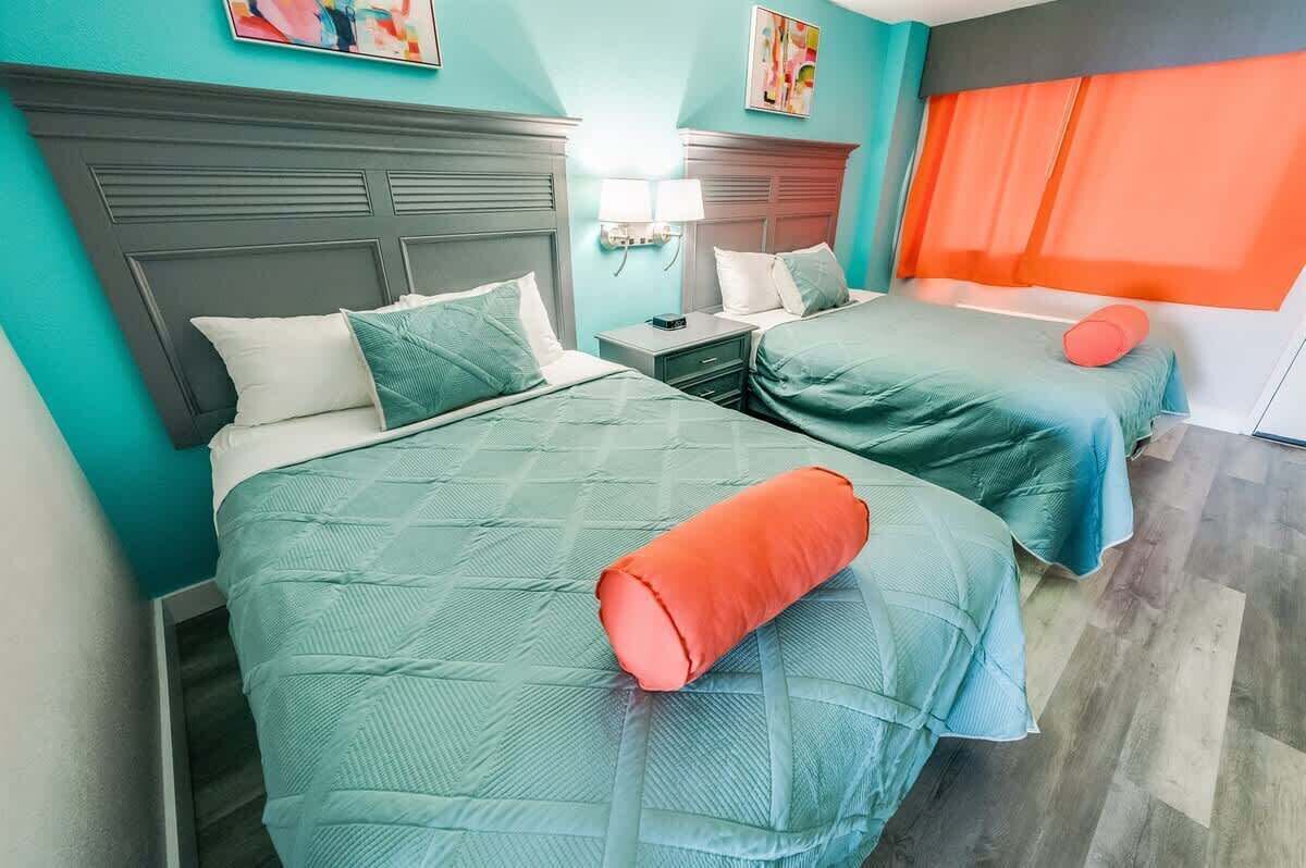 Habitación de hotel con dos camas, cada una con cabecera, mesita de noche y lámpara.