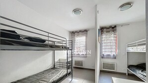 Une chambre de dortoir avec des lits superposés, un bureau, une chaise, un radiateur et une fenêtre avec des rideaux.