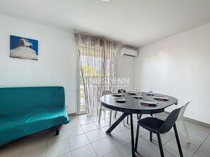 A room with a round dining table, black chairs, a teal sofa, and a window with curtains.