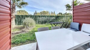 Une terrasse avec une table et des chaises blanches, une haie verte et des palmiers.