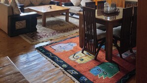 A spacious living room with a wooden staircase, large windows, a dining area, and a patterned rug. - Aananda-Boutique Stays Manali
 (Manali)
