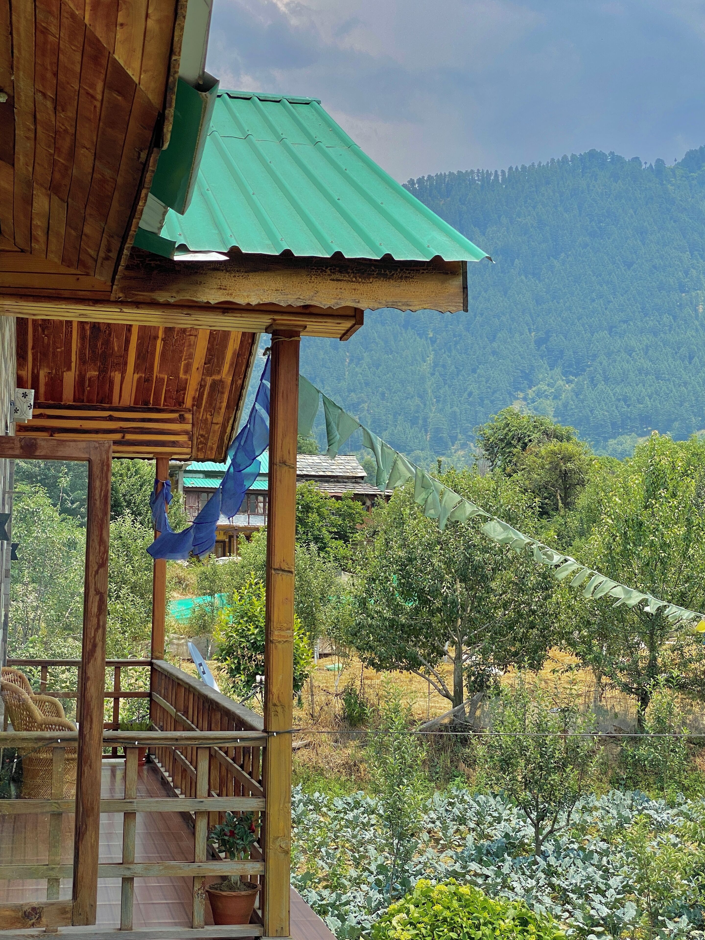 A wooden structure with a green roof, a wooden staircase, and a view of a mountainous landscape with trees and a fence.