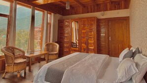 A wooden cabin bedroom with a large bed, wicker chairs, and a view of the mountains through large windows. - Aananda-Boutique Stays Manali
 (Manali)