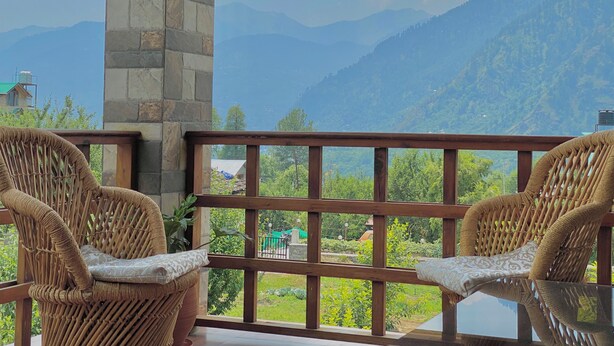 A balcony with wicker chairs and a glass table, overlooking a mountainous landscape. - Aananda-Boutique Stays Manali
 (Manali)