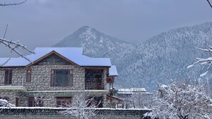 A stone building with a snow-covered roof, set against a backdrop of snow-covered mountains. - Aananda-Boutique Stays Manali
 (Manali)