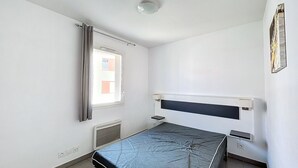 Pieni, siisti huone, jossa on yksi sänky, ikkuna verhoilla, patteri ja seinälle asennettu ilmastointilaite.