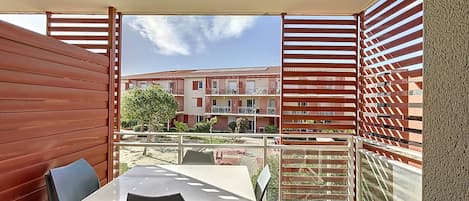 Un balcón con mesa y sillas, vistas de un edificio con balcones y cielo despejado.