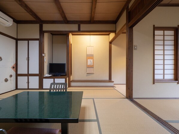 Une pièce de style japonais traditionnel, avec un sol recouvert de tatamis, une table basse en tatami, un téléviseur posé sur un meuble bas et des portes coulissantes.
