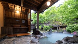 Un onsen japonés tradicional con un vestuario de madera, un sendero de piedra y un entorno natural con árboles y rocas.