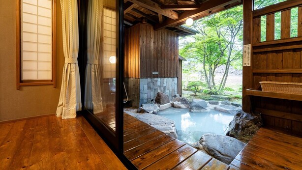 Una habitación tradicional japonesa con suelo de madera y puerta corredera de vidrio que da a un área de aguas termales de piedra.