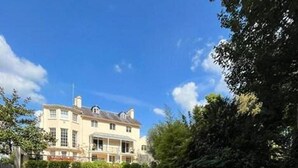 Ein großes, zweistöckiges Gebäude mit symmetrischer Fassade, einem markanten Eingangsbereich mit einer Veranda und einem gepflegten Rasen im Vordergrund.