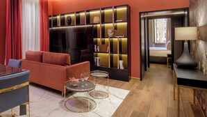 Une chambre d’hôtel moderne avec un canapé rouge, une table à manger, deux petites tables rondes, une bibliothèque et une lampe.