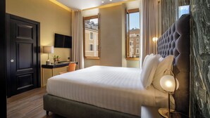 Une chambre d’hôtel avec un grand lit, un bureau avec une lampe, une vue sur les immeubles par la fenêtre et un mur en marbre.