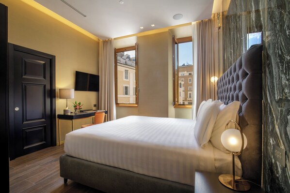 A hotel room with a large bed, a desk with a lamp, a view of buildings through the window, and a marble wall.