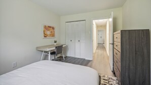 A bedroom with a bed, a desk, a chair, a wardrobe, and a door leading to another room. - Pine Brook 1302 I Pool Gym I Free Parking ! (Newark)