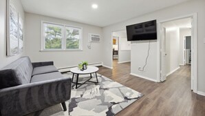 A modern living room with a gray sofa, a round coffee table with a plant, and a large flat-screen TV mounted on the wall.