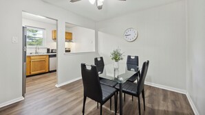 A dining area with a glass table and black chairs, a ceiling fan, and a clock on the wall. - Pine Brook 502 I Pool Gym I Free Parking ! (Newark)