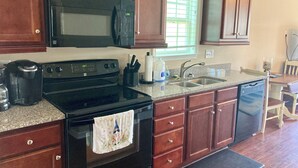 A kitchen with wooden cabinets, a black microwave, a stove, and a dishwasher. - Beach front vacation house (Myrtle Beach)