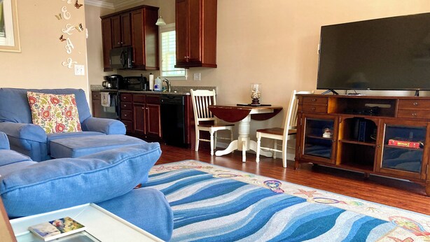 A living room with a blue sofa, a dining area with a white table and chairs, a kitchen with wooden cabinets, and a flat-screen TV on a wooden cabinet. - Beach front vacation house (Myrtle Beach)