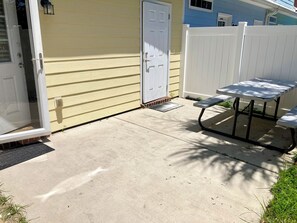 Un patio de concreto con una puerta blanca, una valla blanca y una mesa de picnic.