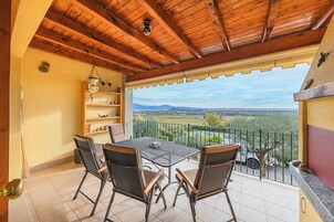 A balcony with a wooden ceiling, a table with chairs, and a view of a rural landscape.