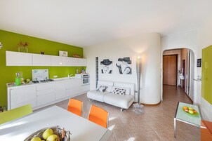 A modern kitchen with white cabinets, a dining table with orange chairs, and a sofa.