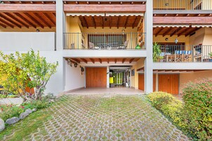A courtyard with a cobblestone floor, a wooden pergola, and a balcony with outdoor furniture.