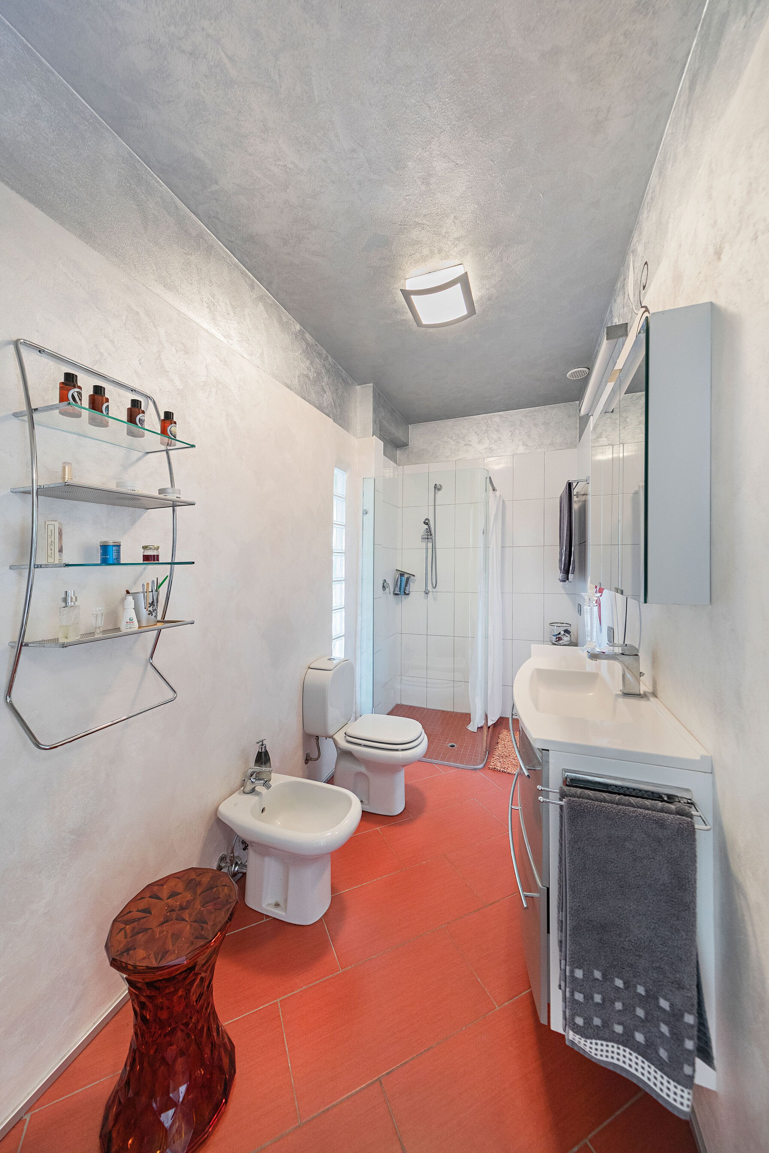 A bathroom with a glass shelf, a toilet, a bidet, a sink, and a mirror.
