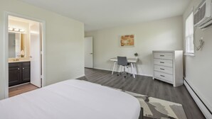 Un dormitorio con cama, escritorio, silla, cómoda y baño con tocador y espejo.