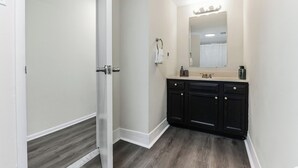 Un baño con puerta blanca, un espejo, un lavabo y armarios de madera oscura.