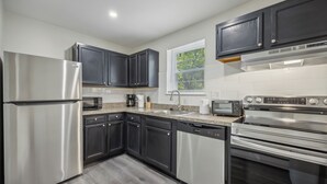 A modern kitchen with stainless steel appliances, dark cabinetry, and a window with blinds. - Pine Brook Apartments: Luxurious living in a stunning wooded setting (Newark)
