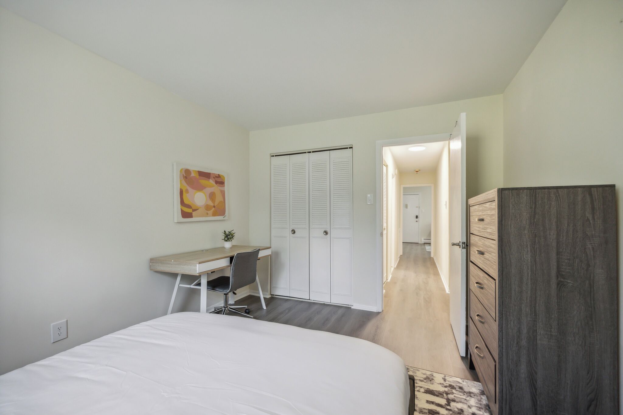Un dormitorio con cama, escritorio, silla, armario y puerta que da a otra habitación.