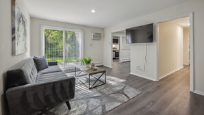 A modern living room with a sofa, coffee table, and a TV mounted on the wall. - Pine Brook Apartments: Luxurious living in a stunning wooded setting (Newark)
