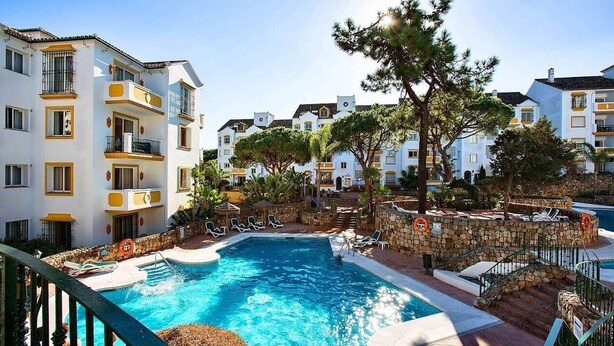 A swimming pool surrounded by multi-story buildings with balconies, stone walls, and outdoor seating areas. - Aparthotel Ona Alanda club, luxury.40 meters from the beach.spectacular views. (Marbella)