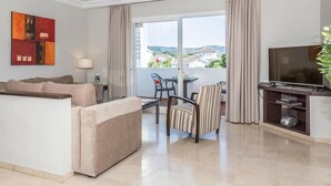 A modern hotel room with a sofa, a dining table with chairs, a TV, and a balcony with a view of buildings and greenery. - Aparthotel Ona Alanda club, luxury.40 meters from the beach.spectacular views. (Marbella)