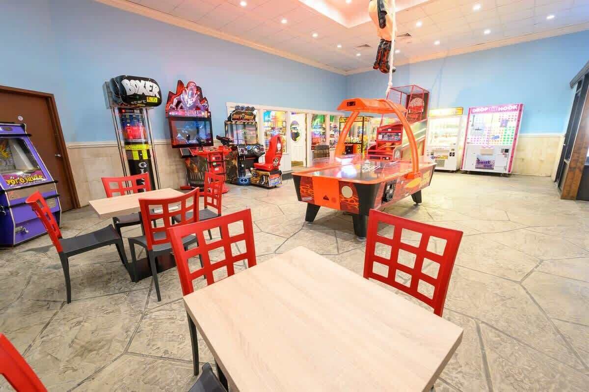 A gaming arcade with various machines, red chairs, and tables.