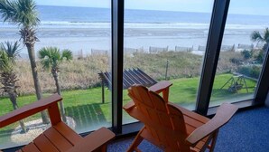 A room with large windows overlooking a beach, featuring two wooden chairs and a swing set. - Oceanfront Studio - Indoor Pools, Hot Tubs, Nice! (Myrtle Beach)