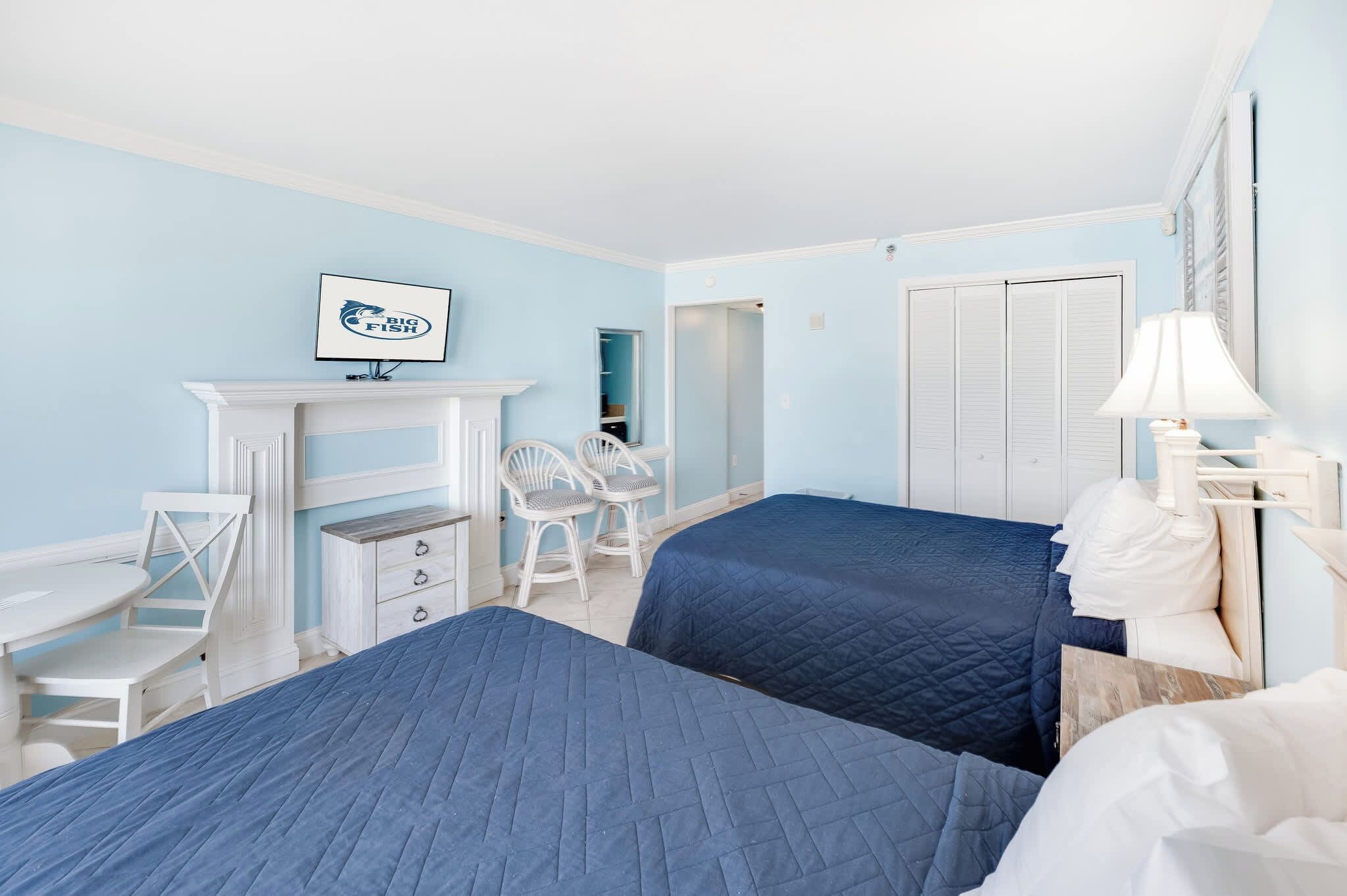A hotel room with two beds, a desk, a chair, a wardrobe, and a framed picture on the wall.