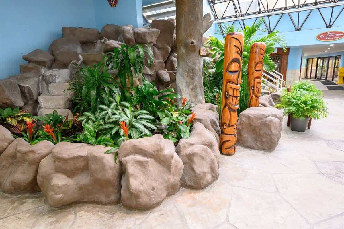 A tropical-themed indoor garden with rock formations, lush green plants, and wooden totem poles.