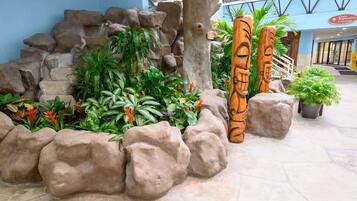 A tropical-themed indoor garden with rock formations, lush green plants, and wooden totem poles.