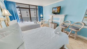 A hotel room with two beds, a TV, a fireplace, and a balcony with blue curtains. - Oceanfront Studio - Indoor Pools, Hot Tubs, Nice! (Myrtle Beach)