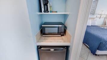 A compact kitchenette with a microwave, a coffee maker, and a small shelf with items.