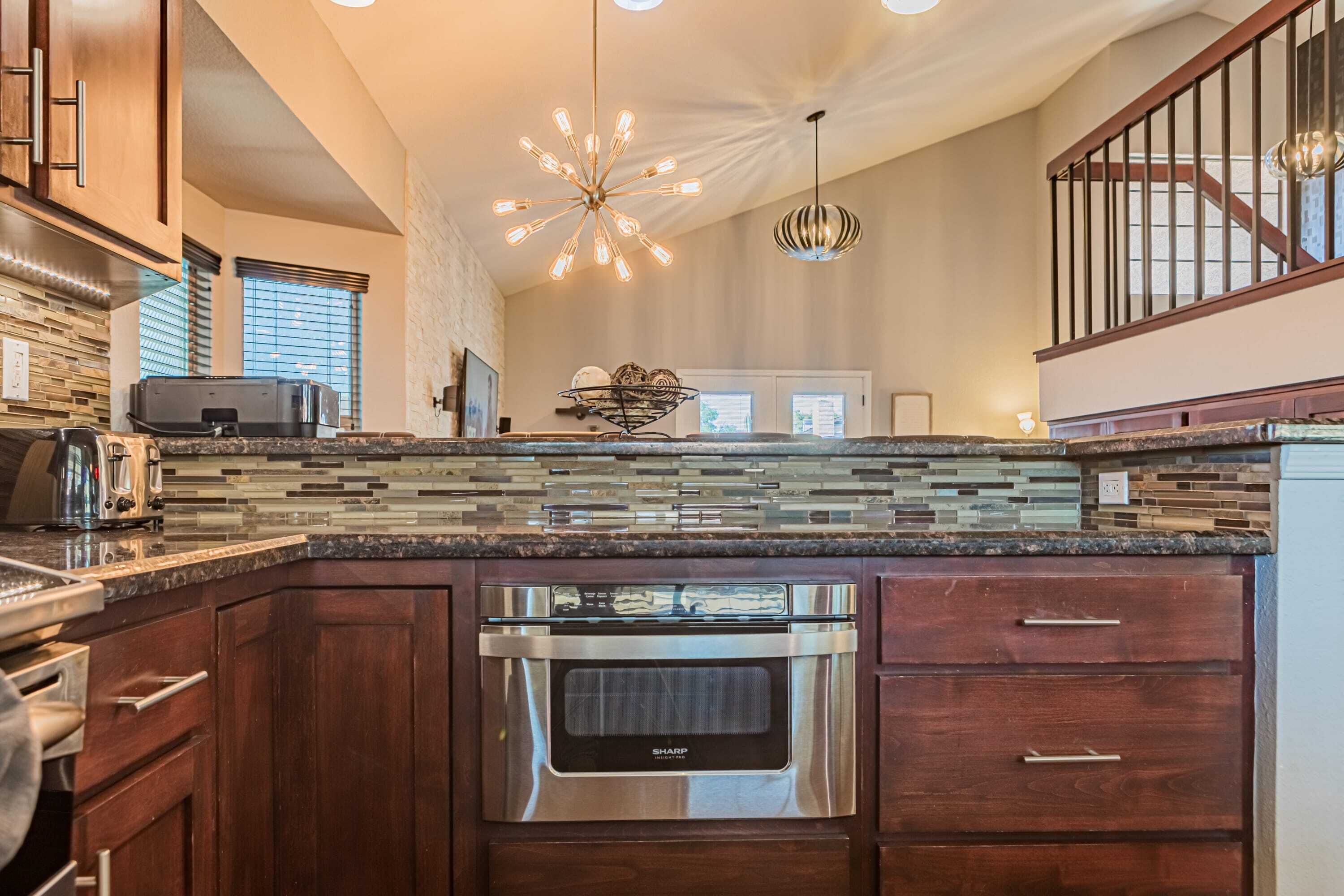 A modern kitchen with a built-in oven, a stone backsplash, and a stainless steel range hood.