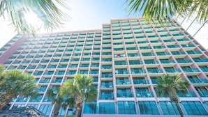 Un grand hôtel avec de nombreux étages, des balcons et des palmiers au premier plan.