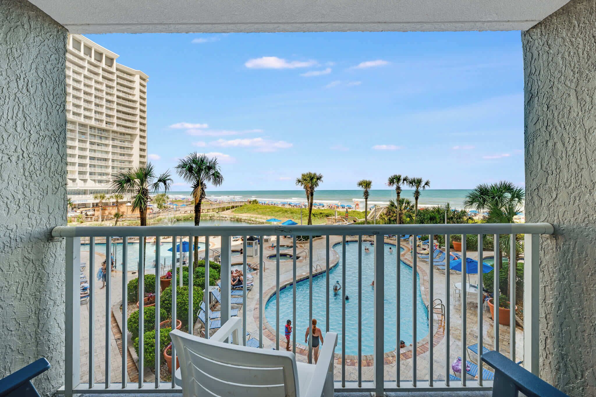 Un balcon avec vue sur une piscine, des palmiers et une plage.